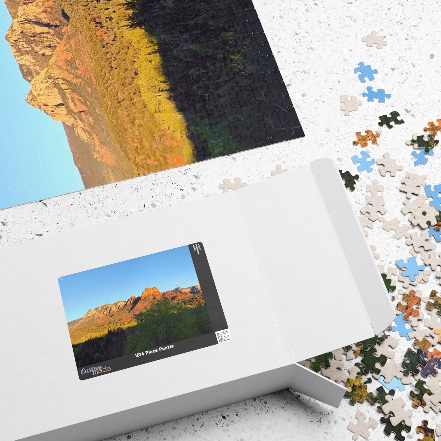Jigsaw puzzle with a mountain landscape design, partially completed, on a white surface. Brilliantmischief.shop